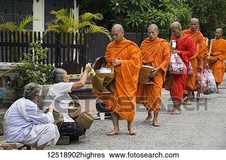 Stock Photograph - Buddhist monks receiving alms on Khounsua Road at dawn; Luang Prabang, Luang Prabang, Laos. Fotosearch
