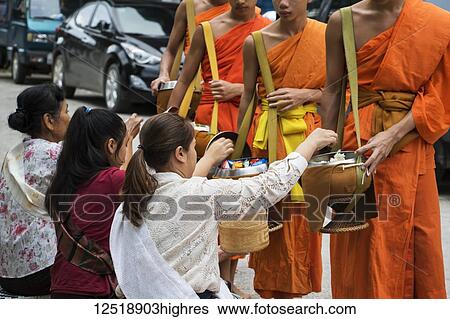 Stock Photograph - Buddhist monks receiving alms on Khounsua Road at dawn; Luang Prabang, Luang Prabang, Laos. Fotosearch