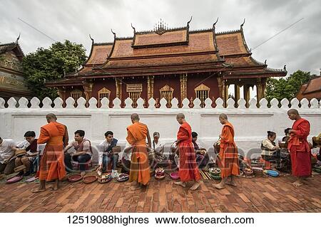 Stock Photograph - Buddhist monks receiving alms on Sisavangvong Road at dawn; Luang Prabang, Luang Prabang, Laos. Fotosearch