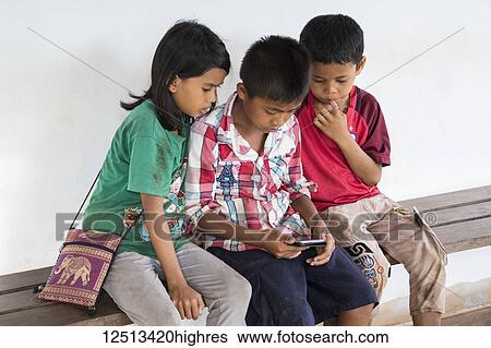Cambodian children looking at a mobile phone; Banteay Srei, Angkor, Siem Reap, Cambodia View Large Photo Image Stock Photograph - Cambodian children looking at a mobile phone; Banteay Srei, Angkor, Siem Reap, Cambodia. Fotosearch
