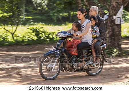 Stock Photograph - Cambodian family riding a motorcycle, Beng Meala; Siem Reap, Cambodia. Fotosearch