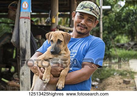 Stock Photograph - Cambodian man holding a dog; O Sra Lav, Battambang, Cambodia. Fotosearch
