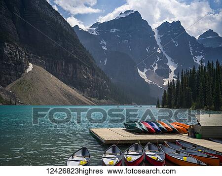Stock Photograph - Canoes in the water and sitting on a dock along the shore of Moraine Lake in the Canadian Rocky Mountains; Eldon, Alberta, Canada. Fotosearch