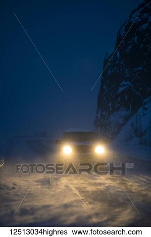 Stock Photograph - Car headlights illuminate the blowing snow on the Seward Highway during a dark winter night, Kenai Peninsula, South-central Alaska; Alaska, United States of America. Fotosearch