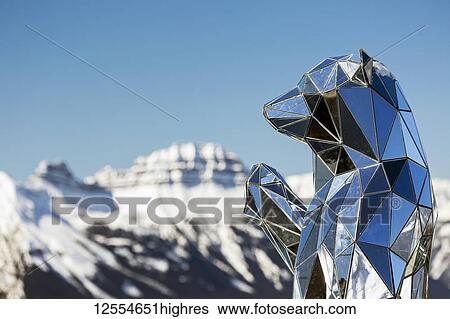 Stock Photograph - Close-up of mirrored bear sculpture with snow-covered mountain and blue sky in the background, Banff National Park; Banff, Alberta, Canada. Fotosearch