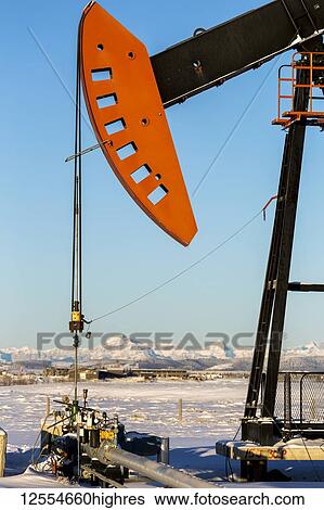 Stock Photograph - Close-up of pumpjack with snow-covered mountains and blue sky in the background, West of Airdrie; Alberta, Canada. Fotosearch