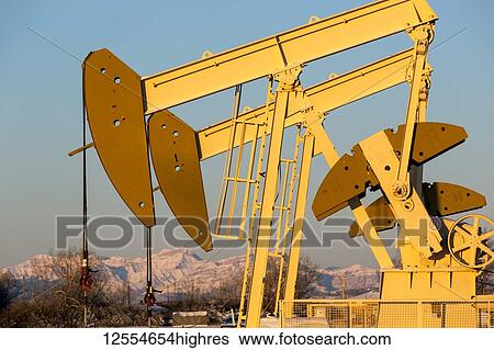 Close-up of pumpjacks with the warm light at sunrise, snow-covered mountains and blue sky in the background, West of Airdrie; Alberta, Canada View Large Photo Image Stock Photograph - Close-up of pumpjacks with the warm light at sunrise, snow-covered mountains and blue sky in the background, West of Airdrie; Alberta, Canada. Fotosearch