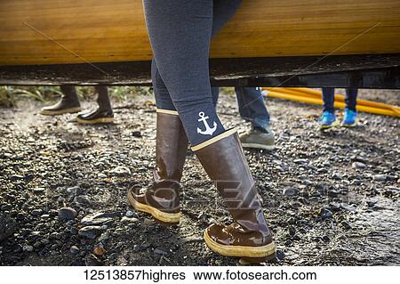 Stock Photograph - Close up of woman walking in rubber boots carrying a wooden boat, South-central Alaska; Homer, Alaska, United States of America. Fotosearch