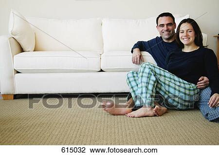Stock Image - Couple hanging out beside sofa. Fotosearch