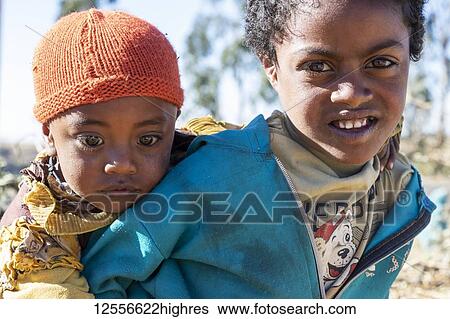 Stock Photograph - Ethiopian girl carrying a little boy, Simien Mountains; Amhara Region, Ethiopia. Fotosearch