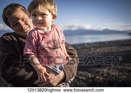 Stock Photograph - Father holds young toddler at sunset along the Homer beach, South-central Alaska; Homer, Alaska, United States of America. Fotosearch