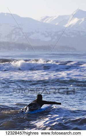 Stock Photograph - Female surfer enters the waters of Kachemak Bay, South-central Alaska; Homer, Alaska, United States of America. Fotosearch