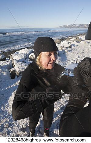 Stock Photograph - Female surfer in wetsuit is poured some water to drink, Homer Spit beach in winter, South-central Alaska; Homer Spit, Alaska, United States of America. Fotosearch