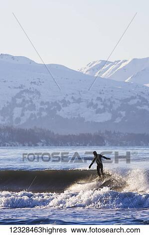 Stock Photograph - Female surfer riding a wave in Kachemak Bay, South-central Alaska; Homer, Alaska, United States of America. Fotosearch