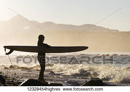 Stock Photograph - Female surfer standing along the wet shore of Kachemak Bay, South-central Alaska; Homer, Alaska, United States of America. Fotosearch