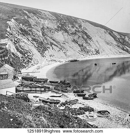 Fishing village on Lulworth Cove with boats on the shore and cliffs along the coast, circa 1900; Devon, England View Large Photo Image Stock Photograph - Fishing village on Lulworth Cove with boats on the shore and cliffs along the coast, circa 1900; Devon, England. Fotosearch