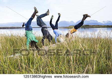 Stock Photograph - Four friends do handstands on a driftwood log along Kachemak Bay, South-central Alaska; Homer, Alaska, United States of America. Fotosearch