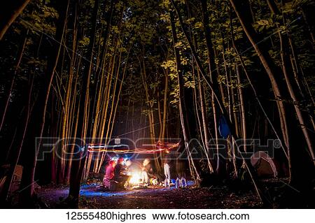 Stock Photograph - Friends playing with lights in a forest at night; Meopham, Kent, England. Fotosearch