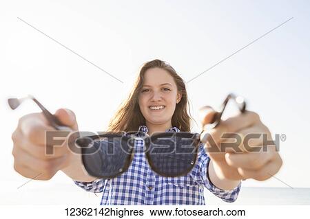 Stock Photograph - Girl offering her sunglasses by holding them out away from her towards the camera, Woodbine Beach; Toronto, Ontario, Canada. Fotosearch
