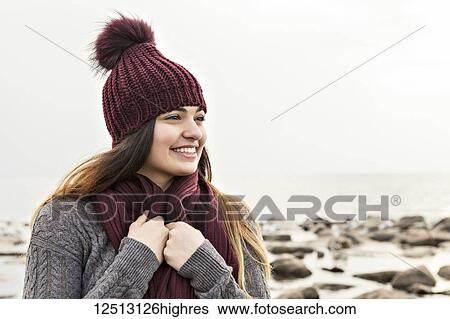 Stock Photograph - Girl standing on a beach in autumn wearing a knit hat and scarf, Woodbine Beach; Toronto, Ontario, Canada. Fotosearch