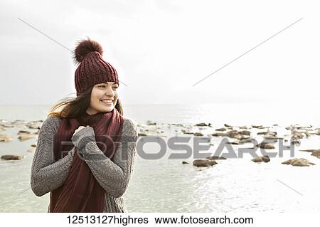 Stock Photograph - Girl standing on a beach in autumn wearing a knit hat and scarf, Woodbine Beach; Toronto, Ontario, Canada. Fotosearch