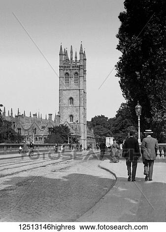 Stock Photograph - Glass Negative circa 1900. Victorian. Social History. A typical village/town street scene in Victorian times. People walking across a bridge, some on bicycles. Tram lines in the road. Fotosearch