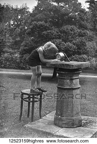 Stock Photograph - Glass Negative circa 1920. Victorian. Social History. A small boy on chair setting his alarm clock using a sun dial. Fotosearch