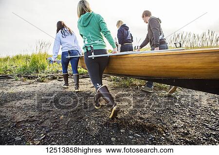 Stock Photograph - Group of young adults carrying a wooden canoe, South-central Alaska; Homer, Alaska, United States of America. Fotosearch