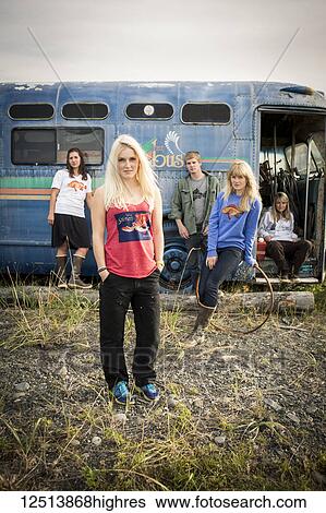 Stock Photograph - Group of young adults hanging out at a vintage rundown bus along coastal Homer, South-central Alaska; Homer, Alaska, United States of America. Fotosearch
