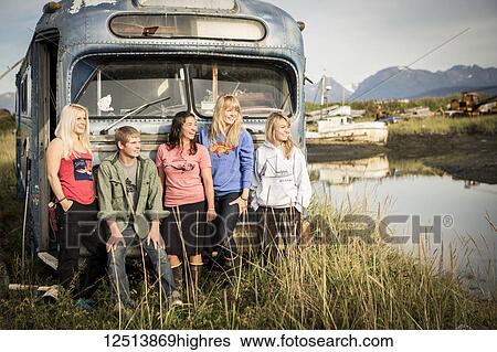 Stock Photograph - Group of young adults hanging out at a vintage rundown bus along coastal Homer, South-central Alaska; Homer, Alaska, United States of America. Fotosearch