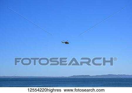 Stock Photograph - Helicopter in a blue sky over the ocean along the coast of Australia; Noosa Heads, Queensland, Australia. Fotosearch