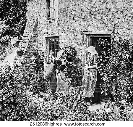 Stock Photograph - Historical image of two women standing outside a stone house talking at the doorway, one coming to sell her wares. Fotosearch