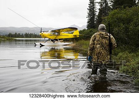 Hunter Wades With His Rife Across His Shoulder In Lake Iliamna With A Piper Super Cub In The Background, Southwest Alaska, USA View Large Photo Image Stock Photograph - Hunter Wades With His Rife Across His Shoulder In Lake Iliamna With A Piper Super Cub In The Background, Southwest Alaska, USA. Fotosearch