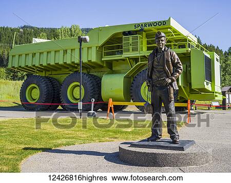Stock Photograph - Large green Titan dump truck on display with a statue of a miner in the foreground; Sparwood, British Columbia, Canada. Fotosearch
