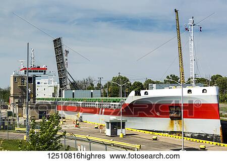 Stock Photograph - Large laker ship going through canal locks with lifted bridge in the background; Port Colborne, Ontario, Canada. Fotosearch