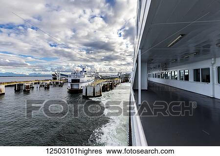 Stock Photograph - Looking over the railing of the passenger deck on BC ferries as the ship leaves the dock at Tsawwassen on a sunny day, another ship is currently in the dock; Vancouver, British Columbia, Canada. Fotosearch