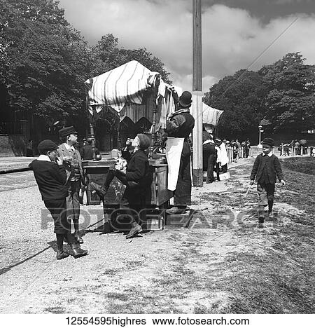 Stock Photograph - Magic lantern slide circa 1880, Victorian/Edwardian Social History. A view of children and people at a market in the park, perhaps an exhibition. The childen are eating sweets and treats.. Fotosearch