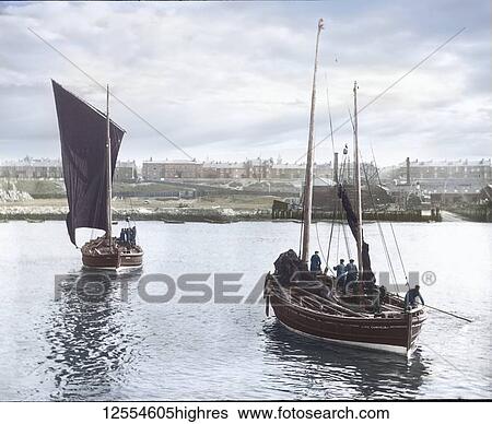 Stock Photograph - Magic lantern slide circa 1880, Victorian/Edwardian Social History. Two fishing boats leaving harbour with South Shields town in the background. Fishermen can be seen on their sail fishing boats preparing for sea; South Shields, Tyne and Wear, England. Fotosearch