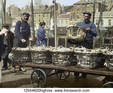 Stock Photograph - Magic lantern slide circa 1880., Victorian/Edwardian Social History. A picture of fishermen unloading herring at North Shields Fish Quay. Buildings include the Newcastle Arms, Union Quay. A lady fisherwoman in the background. Lots of baskets of.... Fotosearch