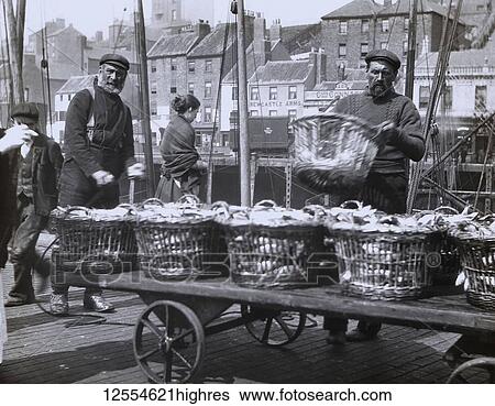 Stock Photograph - Magic lantern slide circa 1880., Victorian/Edwardian Social History. A picture of fishermen unloading herring at North Shields Fish Quay. Buildings include the Newcastle Arms, Union Quay. A lady fisherwoman in the background. Lots of baskets of.... Fotosearch