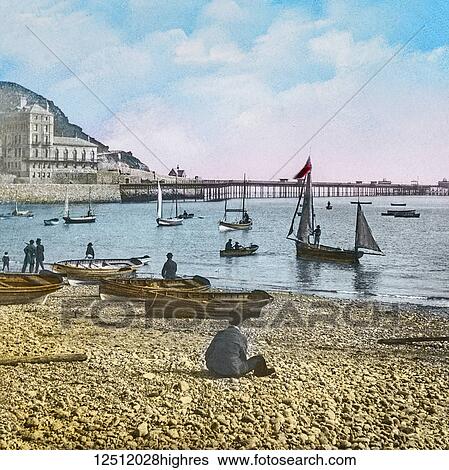 Stock Photograph - Magic Lantern slide circa 1900 hand coloured. created in 1887. A tour of North Wales. 2 Llandudnothe Beach and Pier. Here of good boating here, and a sail round the Great Orme is very pleasant on a fine day, when the excursionist will find much to.... Fotosearch