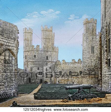 Stock Photograph - Magic Lantern slide circa 1900 hand coloured. created in 1887. A tour of North Wales. 25. Caernarfon Castle Carnarvon CastleInterior. Here we have a view of the interior, which is in a good state of preservation. The walls are nearly eight feet in.... Fotosearch