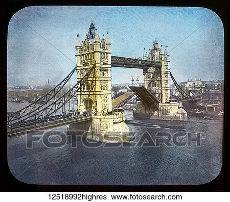 Stock Photograph - Magic Lantern slide circa 1900 hand coloured views of London, England in Victorian times. Slide 13 Tower Bridge London. The bridge halfway up with people and traffic crossing. Fotosearch