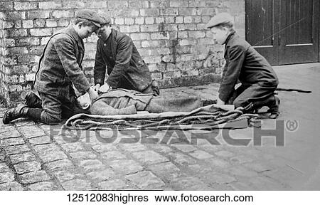 Stock Photograph - Magic lantern slide circa 1900. Victorian. Social History. Street children practicing first aid on another little boy. Fotosearch