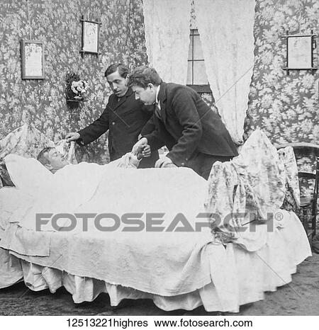 Stock Photograph - Magic lantern slide circa 1900. Victorian. Social History. Image from a slide presentation entitled In His step or In jesus Name. A sick man in his bed wioth the minister and a doctor holding his hand before he dies. Fotosearch