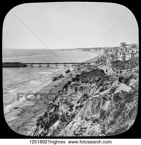 Stock Photograph - Magic lantern slide circa 1900. Victorian/Edwardian. Social History. Bournemouth Pier before 1891. Beach huts and people on the beach. general view. Fotosearch