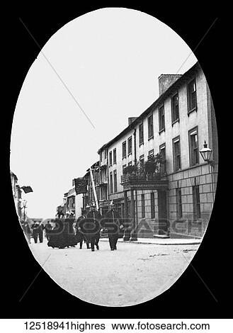 Stock Photograph - Magic lantern slide circa 1900. Victorian/Edwardian. Social History. Two policeman, ladies and gentlemen escorted along the street past the Lion Royal Hotel. Fotosearch