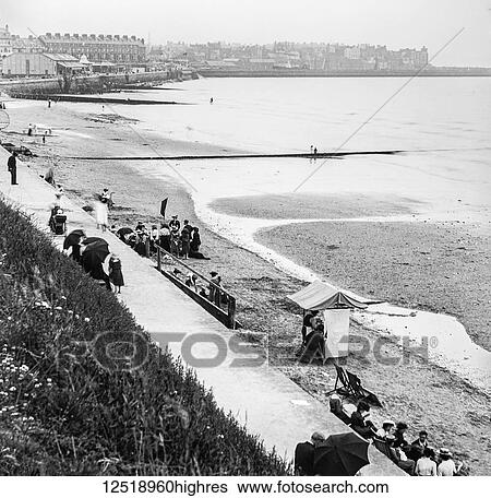 Stock Photograph - Magic lantern slide circa 1900. Victorian/Edwardian. Social History. Bridlington Bay, Princes Parade. A view of the beach, houses and quay with people enjoying a day out. Fotosearch