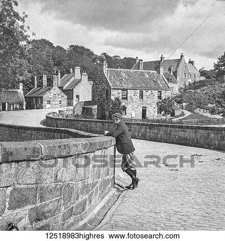 Stock Photograph - Magic lantern slide circa 1900. Victorian/Edwardian. Social History. Man wearing Plus Four trousers standing on bridge in village. Fotosearch