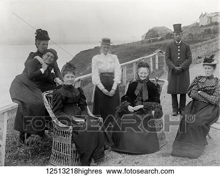Stock Photograph - Magic lantern slide Glass negative. A well to do family on holiday sitting on the cliff tops. The chauffer posing witht he family. Victgorian ladies in bsket chairs. Fotosearch